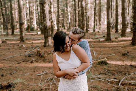 guy kissing girl on cheek hugging her from behind in forest
