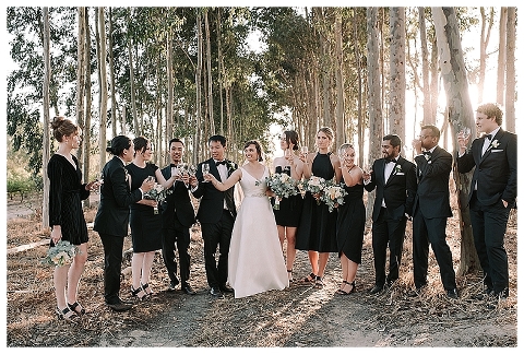 bridal party on dirt track cheers with wine